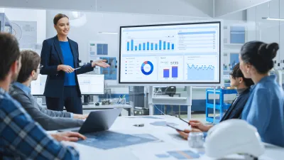 Person in blue jacket presenting data charts to colleagues in modern office meeting room.