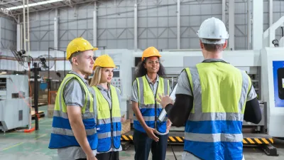 Three workers in hard hats, safety vests, and protective gear discussing at an industrial facility.