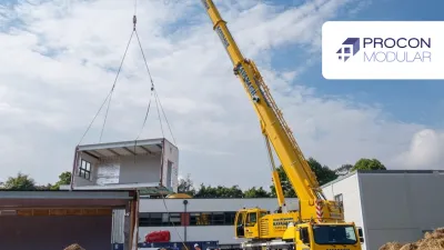 Yellow crane lifting a large modular structure at a construction site under blue sky.