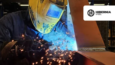 Welder in protective helmet working with bright blue sparks in industrial setting.