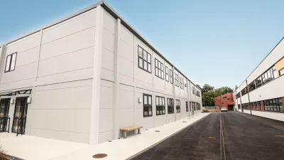 White two-story prefabricated modular building with flat roof against blue sky.