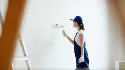 Person in blue cap and tank top painting a wall with a roller
