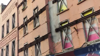 Colorful triangular banners hanging along a pink building facade with graffiti below.