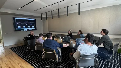 A group of people sitting in a modern meeting room with a large screen displaying content.