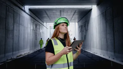 Construction worker in safety vest and green helmet using tablet in concrete tunnel.