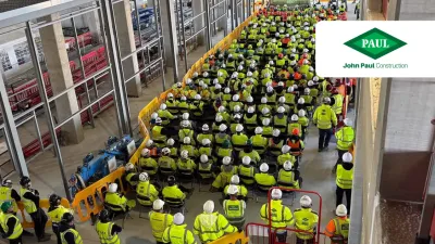 Workers in yellow safety vests in a large warehouse or retail facility with refrigeration units.