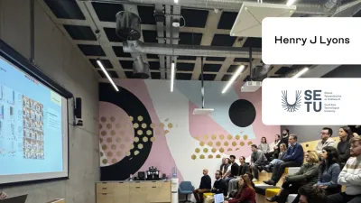 Audience seated in a modern lecture hall with geometric wall designs and digital screens.