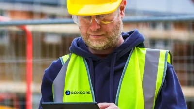 Construction worker in yellow hard hat and safety vest looking at mobile device.