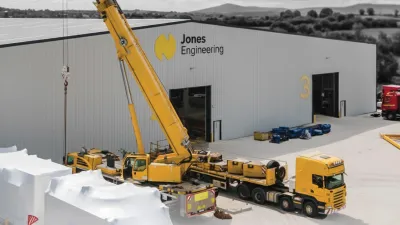 Yellow crane and truck at an industrial building site with white warehouse.