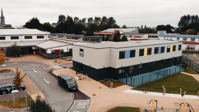 Aerial view of a commercial complex with white buildings, parking lot, and landscaped areas.