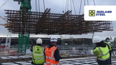 Construction workers in bright safety vests watching a large steel structure being lifted by a crane.