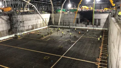 Construction site with concrete foundation, steel rebar grid, and yellow crane at night.