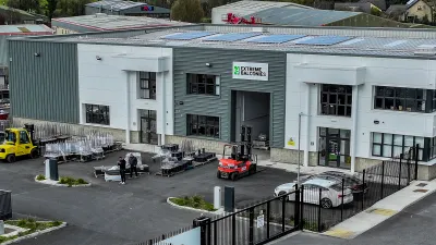Aerial view of an industrial warehouse complex with solar panels, vehicles, and stacked materials outside.