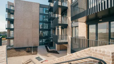 Modern apartment building with brick facade, balconies, and glass railings on an overcast day.
