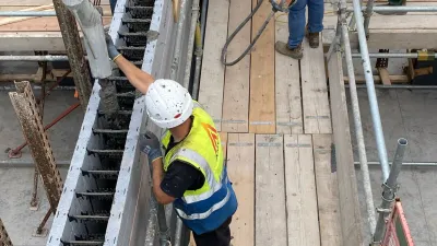 Three construction workers in high-visibility vests and hard hats working on a wooden scaffolding platform.