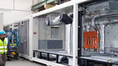 Worker in blue hard hat standing beside large industrial HVAC or processing unit in a factory.
