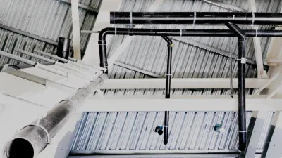 Industrial ceiling with exposed metal ductwork, pipes, and ventilation systems in a large facility.