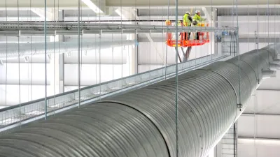 Two workers in safety gear inspecting large industrial ductwork from an elevated platform.