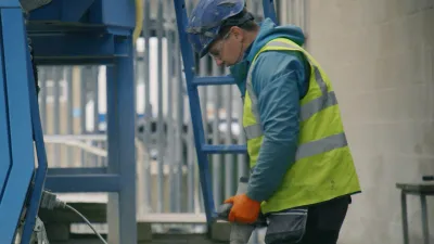 Worker in yellow safety vest and blue hard hat operating industrial equipment.
