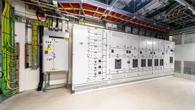 Large industrial electrical control panel room with gray switchgear cabinets and colorful overhead cable trays.