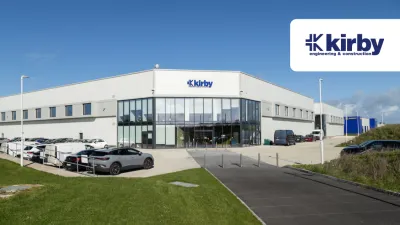 Large modern Kirby industrial building with parked cars outside under a partly cloudy sky.
