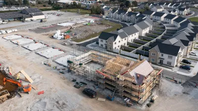 Aerial view of a residential construction site with framed buildings and completed homes nearby.