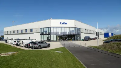 Modern industrial building with "Eleby" signage, cars parked outside under a cloudy sky.