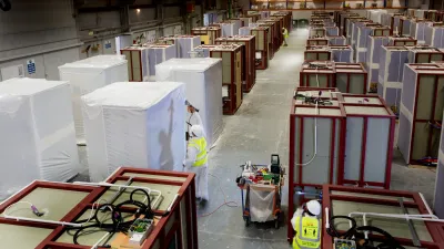 Worker in yellow vest moving through a large warehouse stocked with white panels and red frames.
