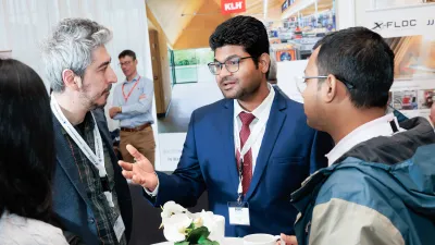 Three men in business attire engaged in conversation at a conference or trade show.