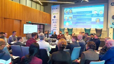Conference room with attendees seated at round tables, facing a large presentation screen.