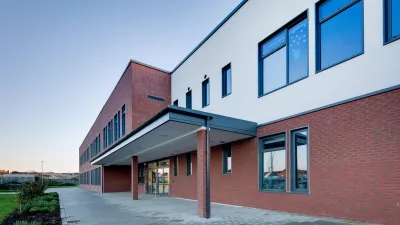 Modern brick and white school building exterior at dusk, with large windows and covered entrance.