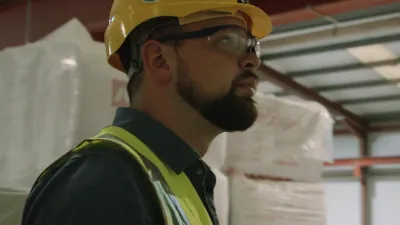 Man wearing a yellow hard hat and safety vest in an industrial warehouse setting.