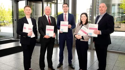 Five professionals standing outside a modern glass building, holding red and white documents.