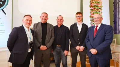 Five men standing together indoors, smiling for a group photo in a formal setting.