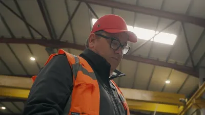 Person wearing a high-visibility vest and red cap reviewing documents inside a manufacturing facility.