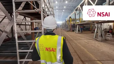 Worker in NSAI yellow vest and hard hat inspecting a large industrial facility.
