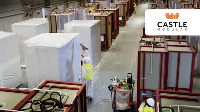 Factory workers preparing prefabricated construction modules inside a large manufacturing facility. Numerous partially assembled modules are arranged throughout the factory floor.