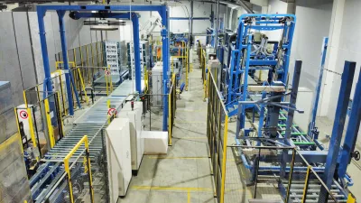 Industrial manufacturing facility with blue metal frames, conveyor systems, and white panels on the floor.