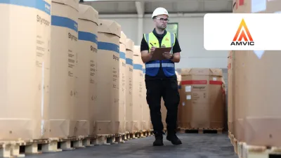 Worker in safety vest and helmet inspecting warehouse inventory with a tablet.