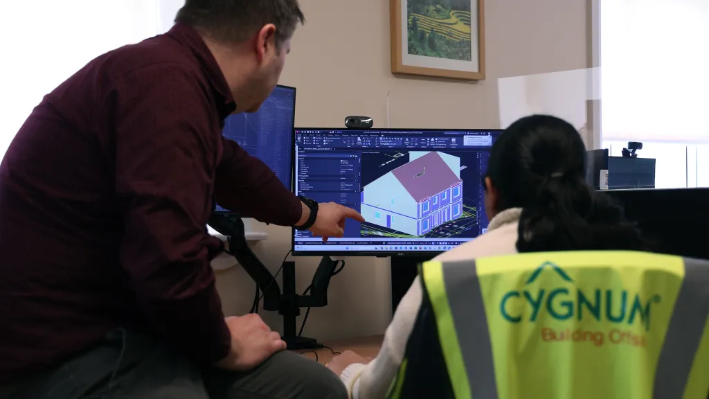 Two people in an office reviewing a 3D building model on a computer screen