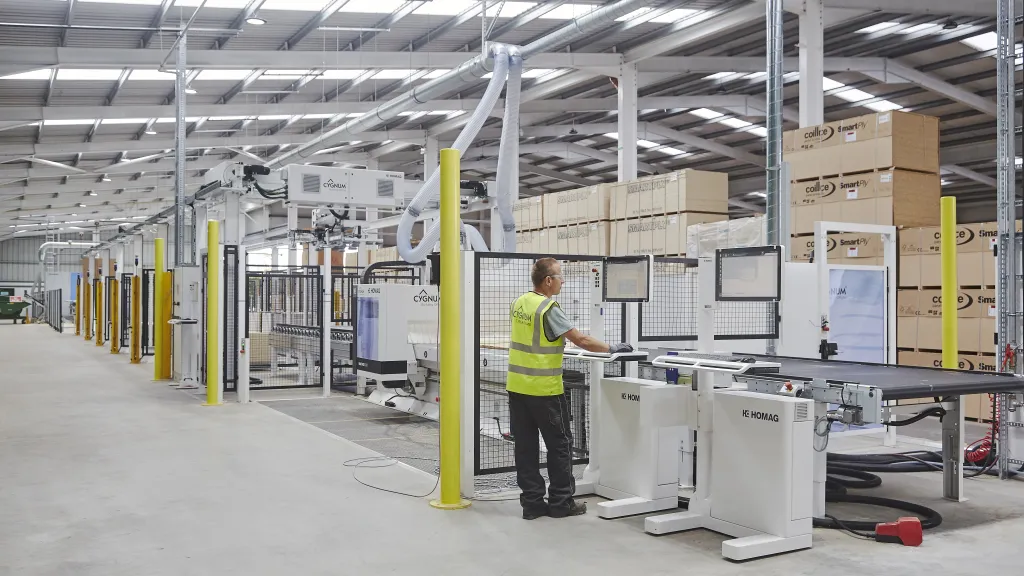 Person in high-vis vest operating a robotic system inside a construction manufacturing facility.