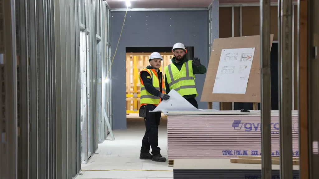 Two people in high-vis vests and hard hats reviewing plans inside a construction unit.
