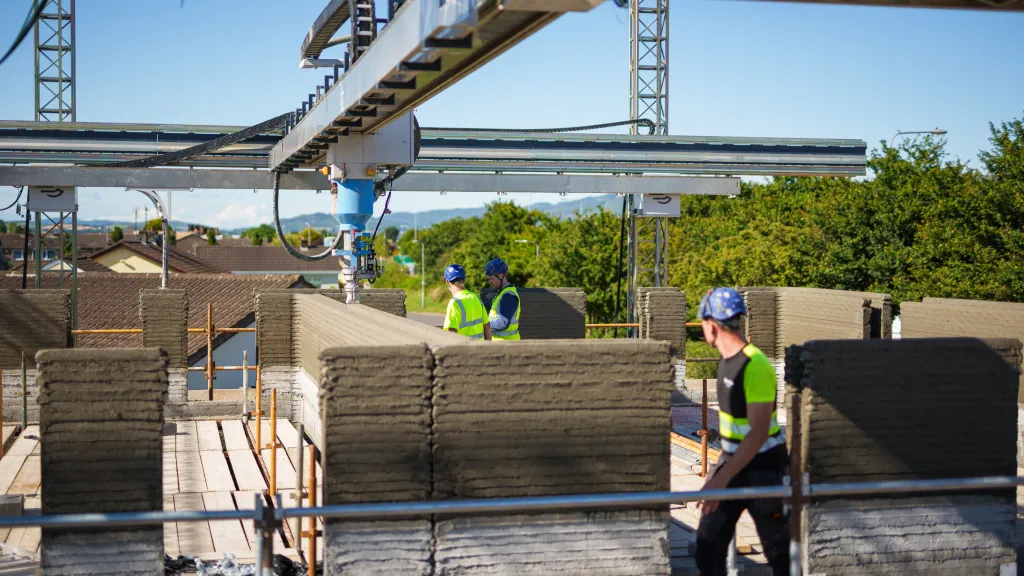 Workers operating a 3D concrete printing machine on a сonstruction site.