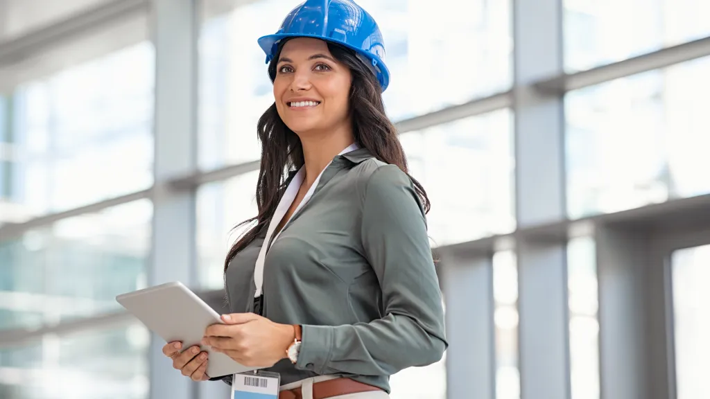 Person wearing a blue hard hat and holding a tablet, standing in a bright modern building.