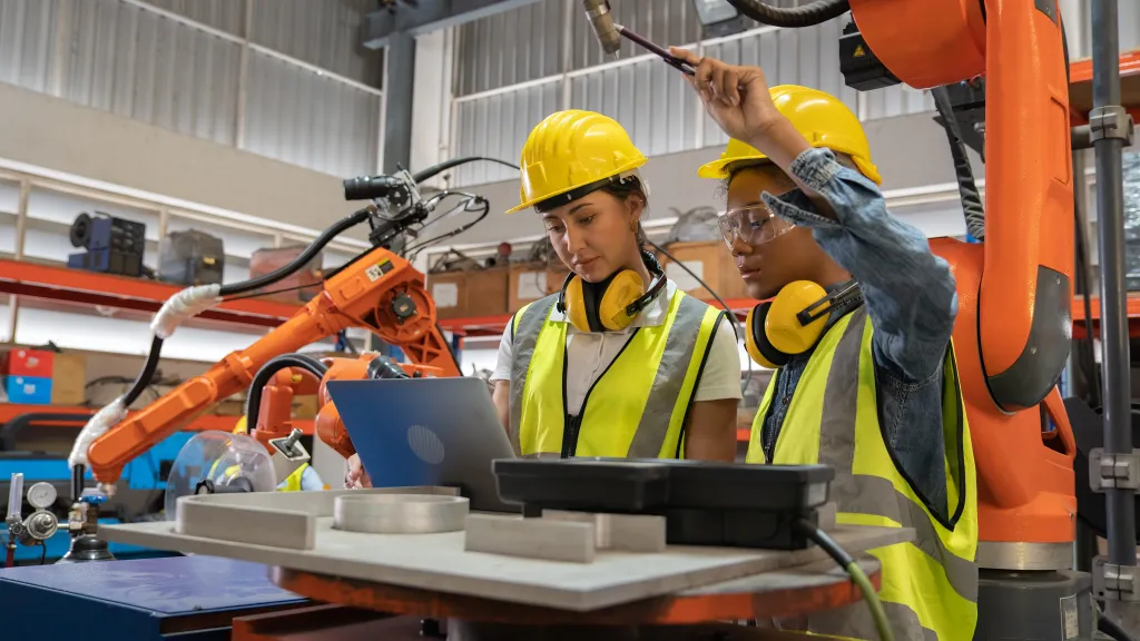 Two workers wearing high-visibility vests and hard hats are working with robotics.