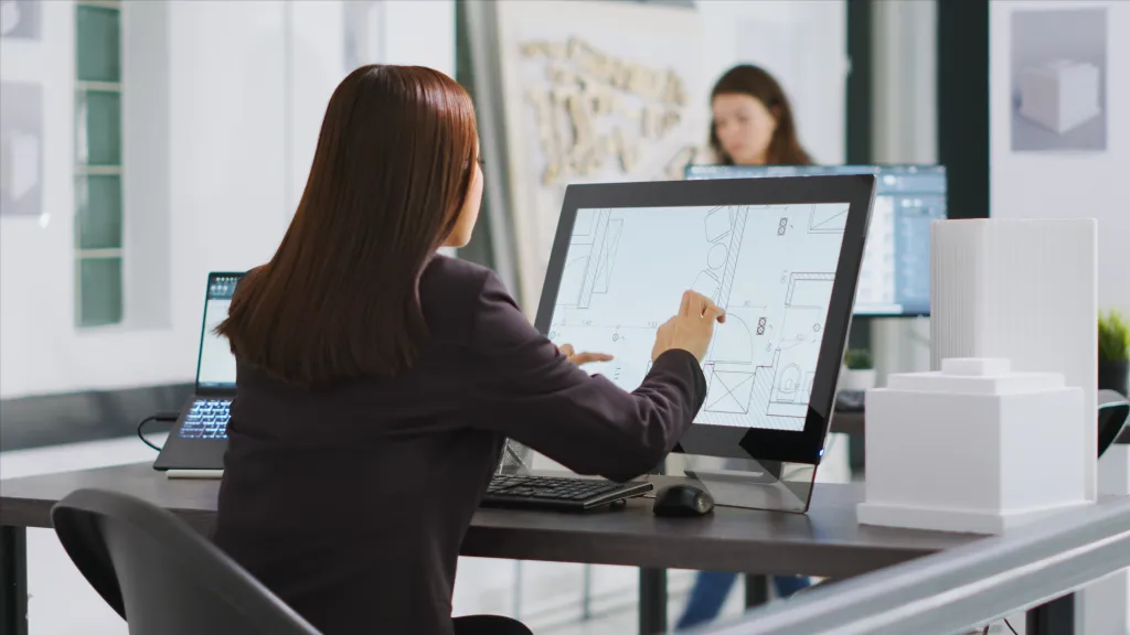 A person is seated in an office working on architectural design using a touchscreen device.
