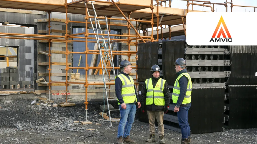 Three construction workers in helmets and safety vests discussing at a building site with scaffolding