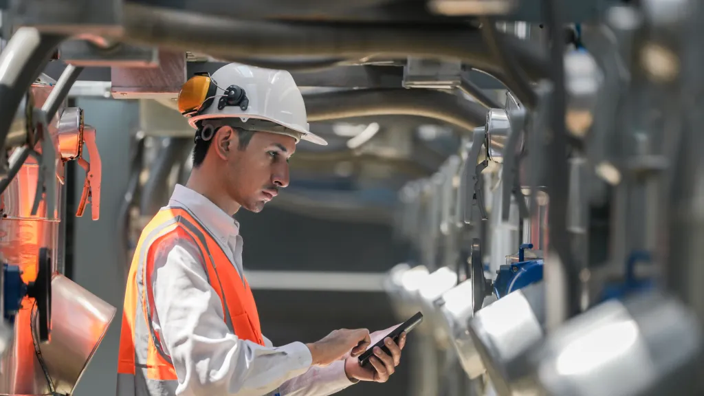A construction worker wearing safety gear using a tablet near machinery.