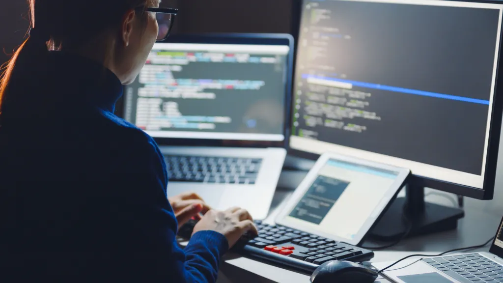 Person working at a desk with multiple screens showing code and data.