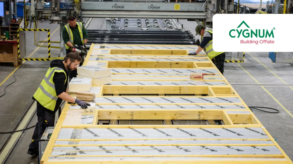 Workers in high-visibility vests assembling insulated timber wall panels inside a modern offsite construction factory.